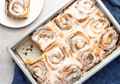 Cinnamon rolls in pan with a roll served on a plate peeking into frame