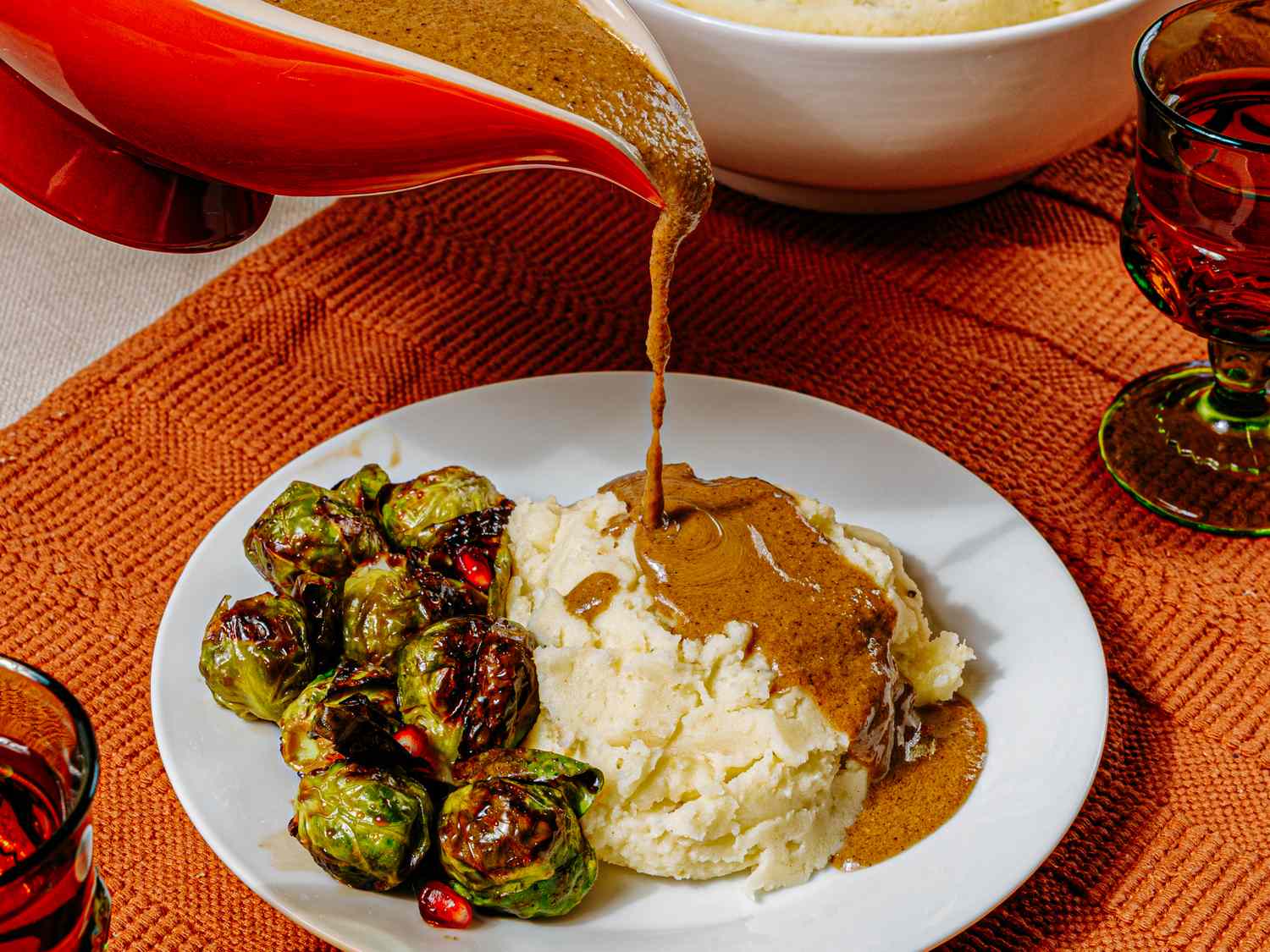 Vegetarian gravy being poured onto mashed potatoes accompanied by roasted Brussels sprouts
