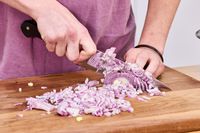 A person chopping an onion on a wooden cutting board using the Wüsthof Classic 8-Inch Chef's Knife