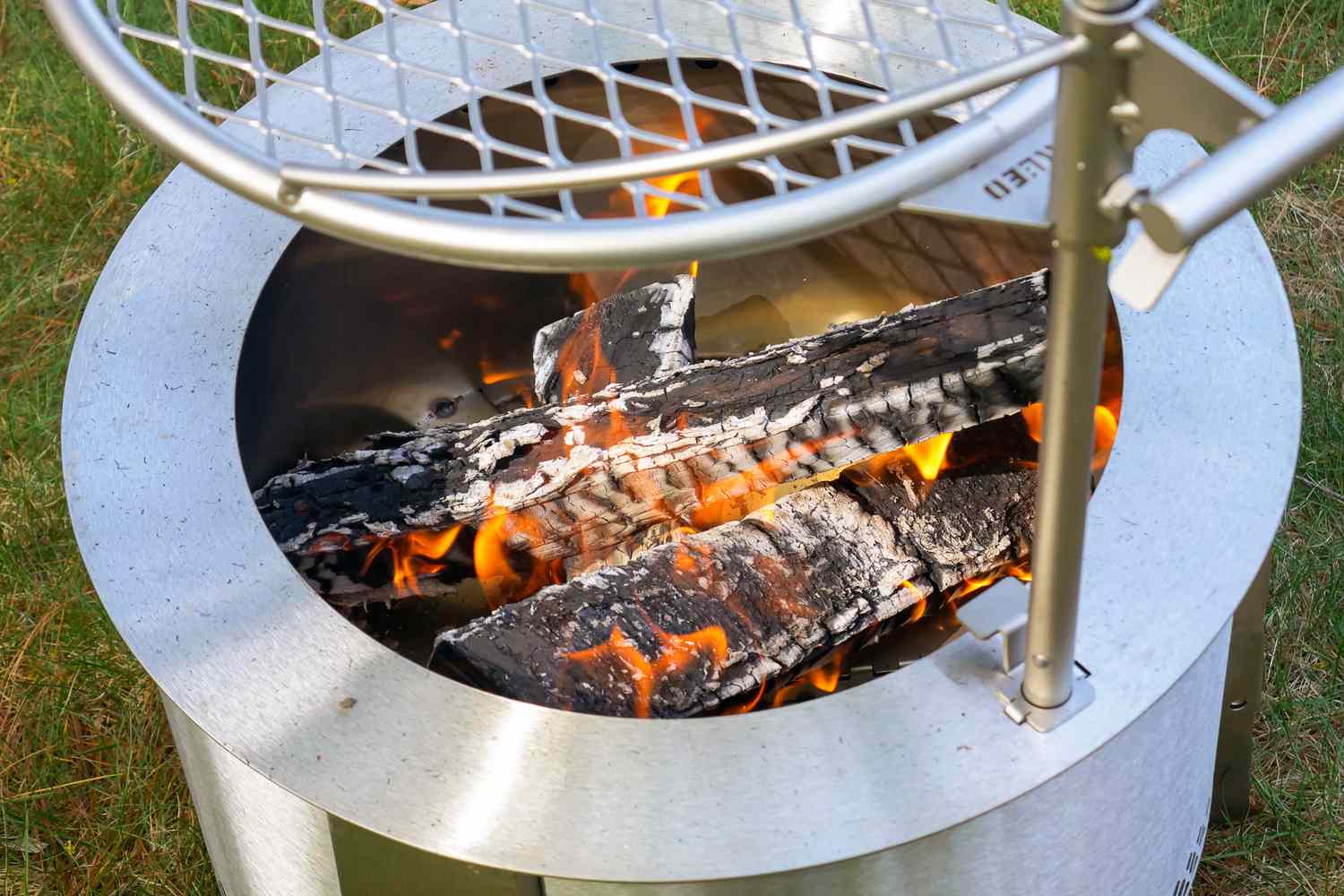 Close-up of a metal fire pit with burning logs and a mesh grill over the top
