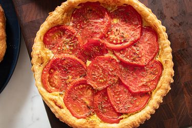 Tomato tart with layered tomato slices on top of a golden crust placed on a wooden surface