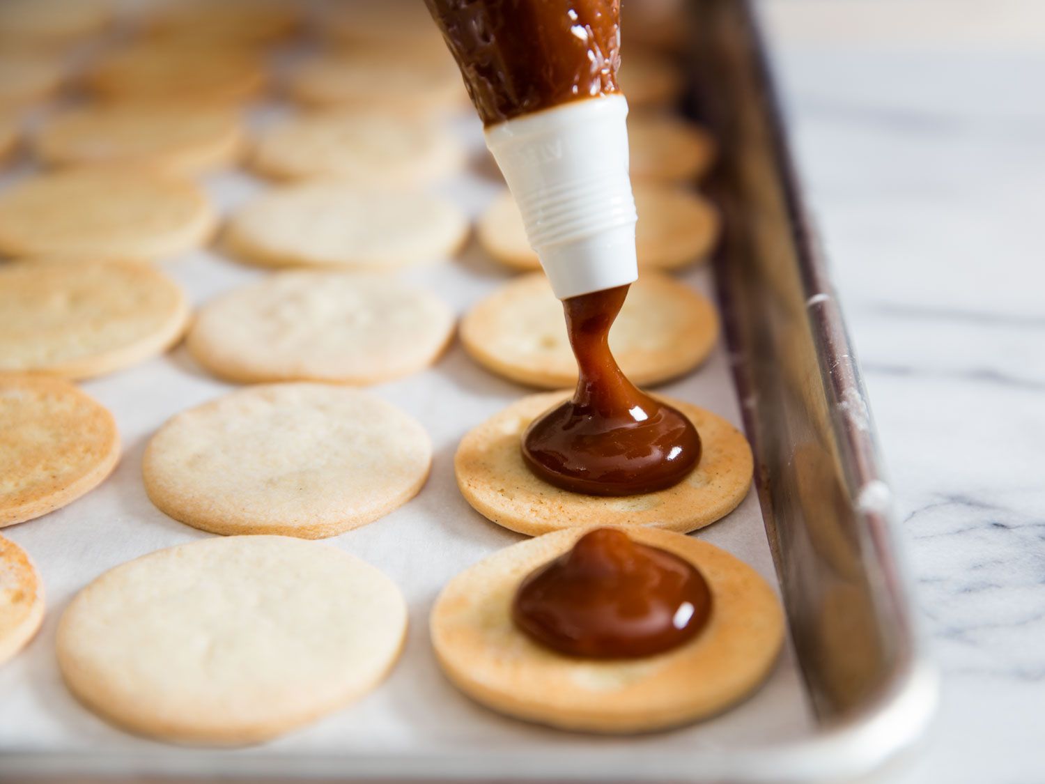 Half of the cookies are flipped over to reveal their flat bottoms and cajeta is portioned onto them with a pastry bag.