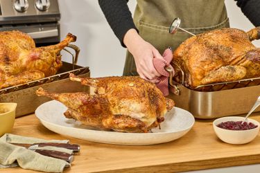 Three cooked turkeys on a kitchen countertop. A person is placing a turkey in a roasting pan onto the countertop.