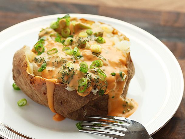 Baked potato topped with broccoli florets, scallions and vegan nacho cheese plated with a fork