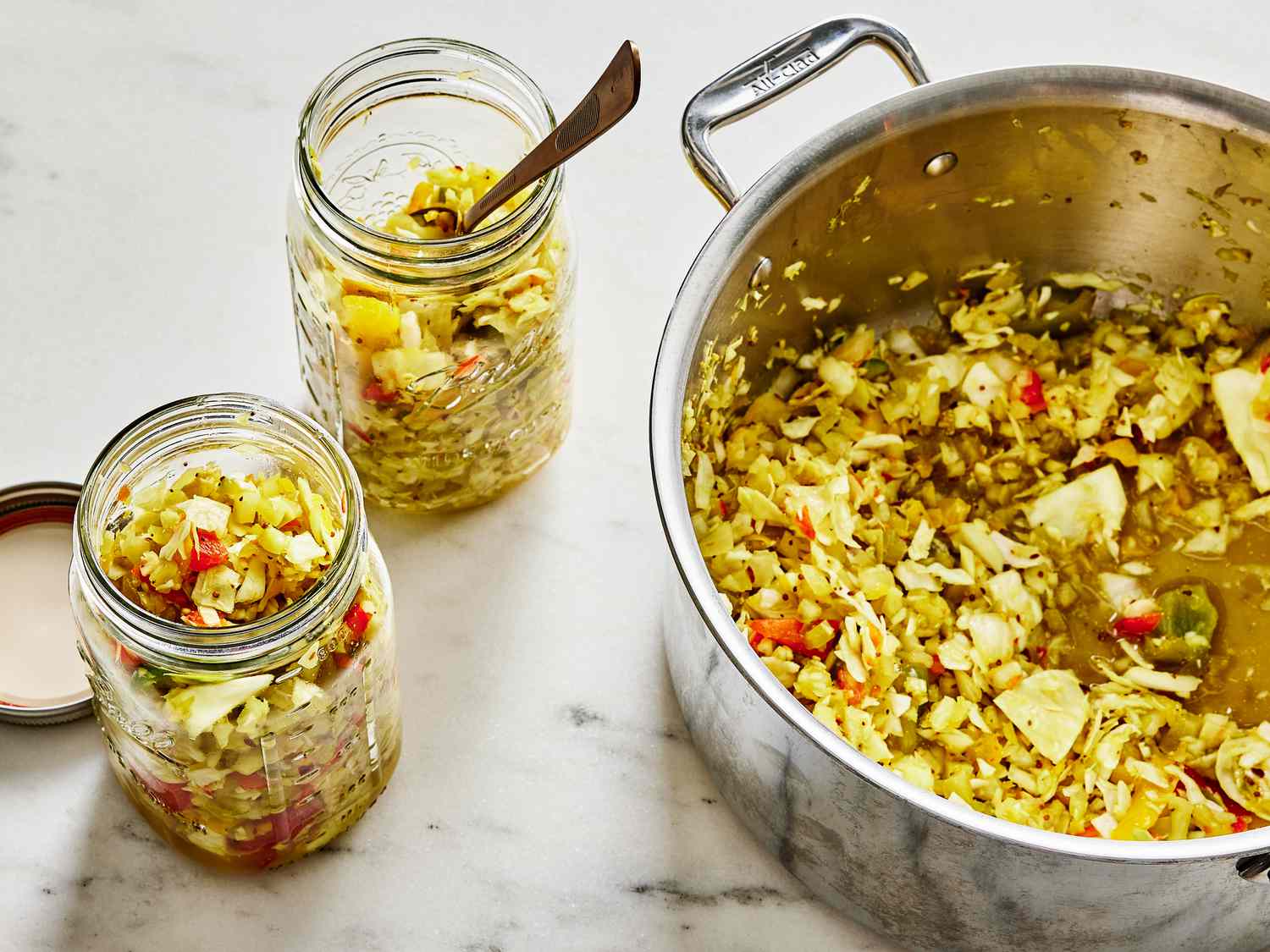 Portions od Chow Chow added into 2 glass jars, pot of more Chow Chow next to glass jars 