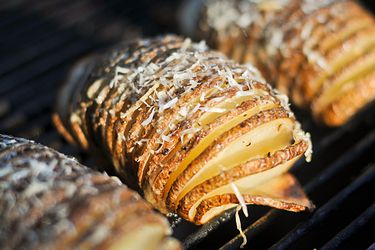 Closeup of Grilled Hasselback Potatoes With Garlic and Parmesan cooking on a grill grate.