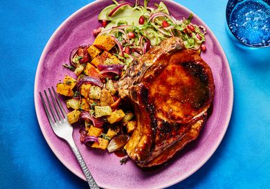 Dish with a glazed pork chop roasted vegetables and a fresh salad on a plate
