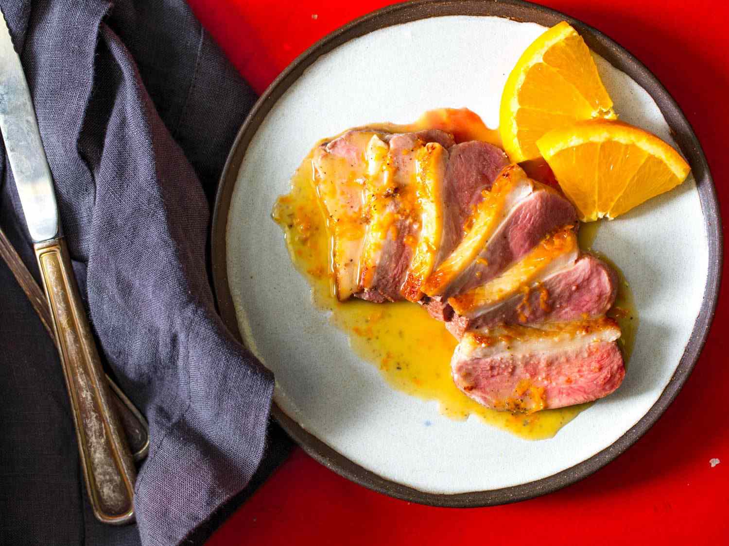 Seared duck breast, sliced and arranged on white plate, served with orange pan sauce and garnished with orange slices