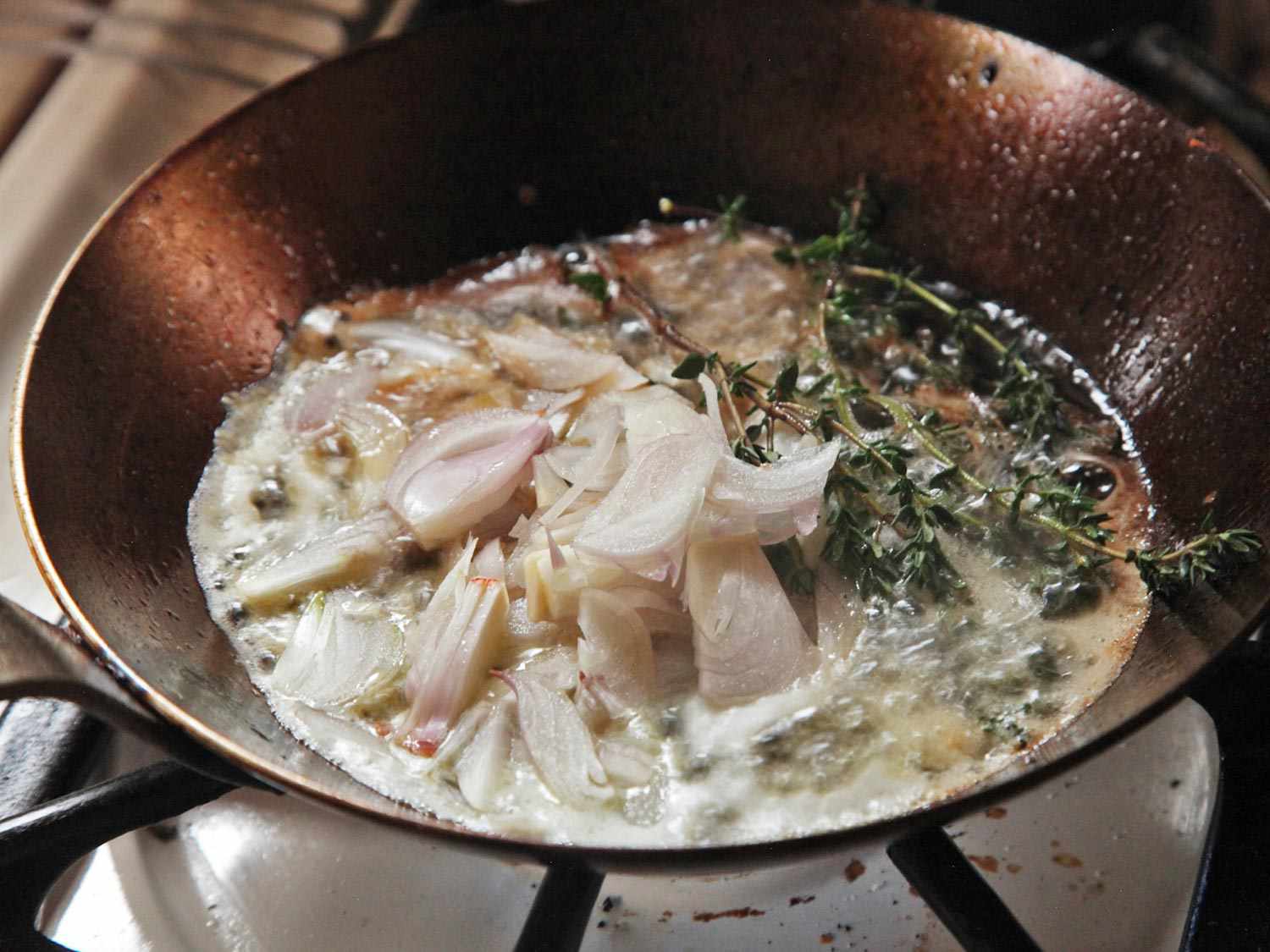 Sliced shallots and fresh thyme browning in butter in a pan