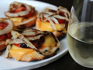 Closeup of a plate of animal-style grilled cheese cruschetta, served with a glass of cold white wine.