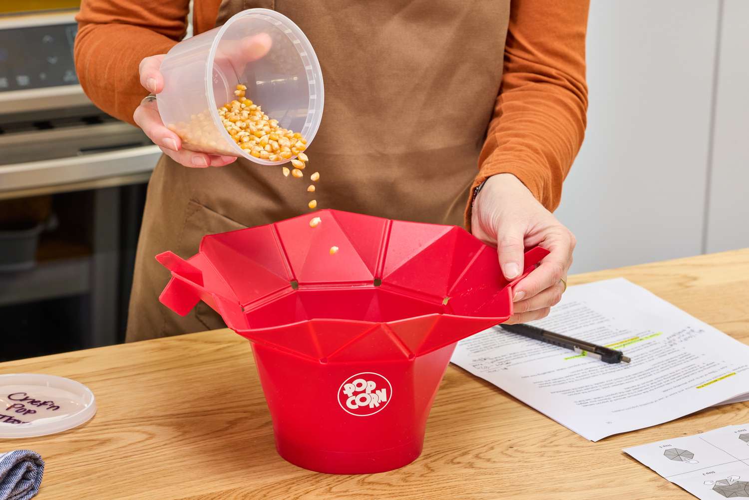 A person pours popcorn kernels into the Chef'n Pop Top Microwave Popcorn Maker