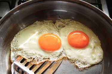 Two fried eggs in a pan with a spatula beneath them