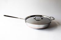 A metal frying pan with a lid long handle on the left and a side handle on the right