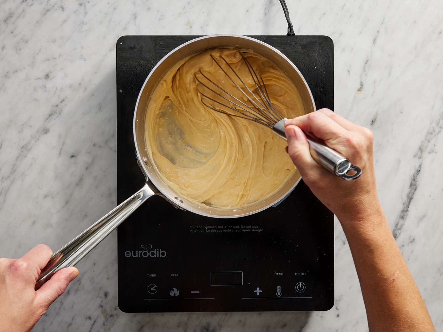 Overhead view of hands mixing cheese sauce on an induction top