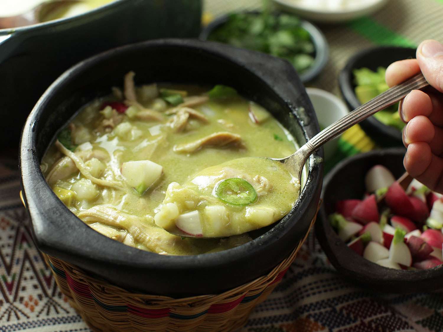 A spoonful of homemade Mexican green pozole lifted from a black bowl.