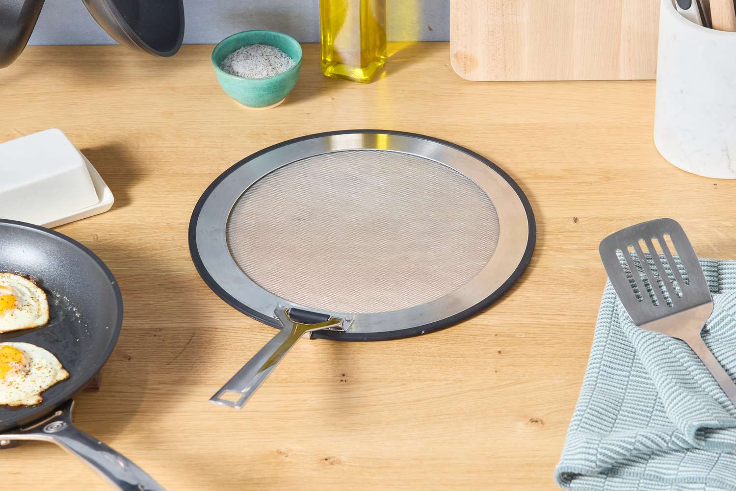 the le creuset splatter screen on a countertop with the handle unfolded 