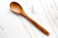 A FAAY Teak Cooking Spoon on a marblelike surface