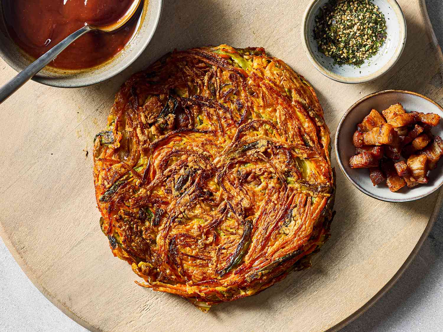 A Japanese okonomiyaki surrounded by condiments and toppings