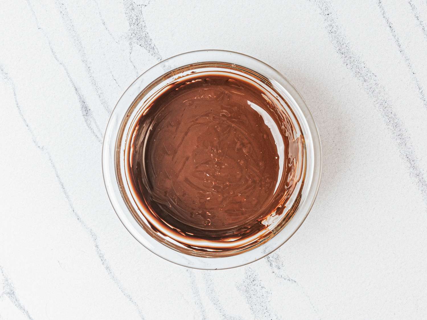 Melted chocolate in a glass bowl on a marble surface