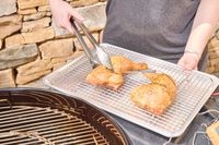 A hand using tongs to move chicken onto a tray from the Weber Performer Deluxe Charcoal Grill 22