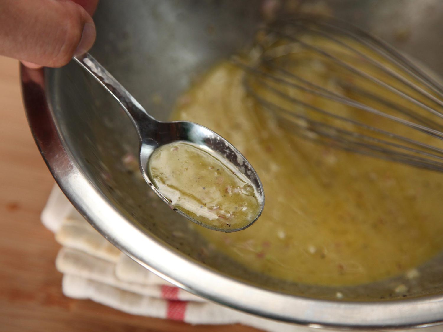 A spoonful of emulsified vinaigrette is held up to the camera.