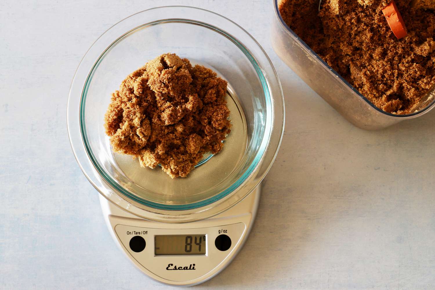 Measuring brown sugar in a glass mixing bowl on a kitchen scale.