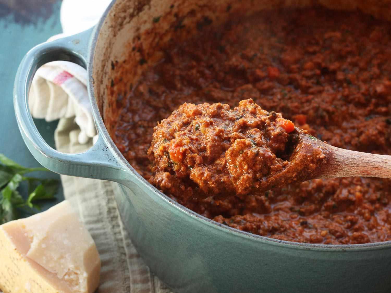 A spoonful of finished Bolognese sauce being held over a pot full of the remaining sauce.