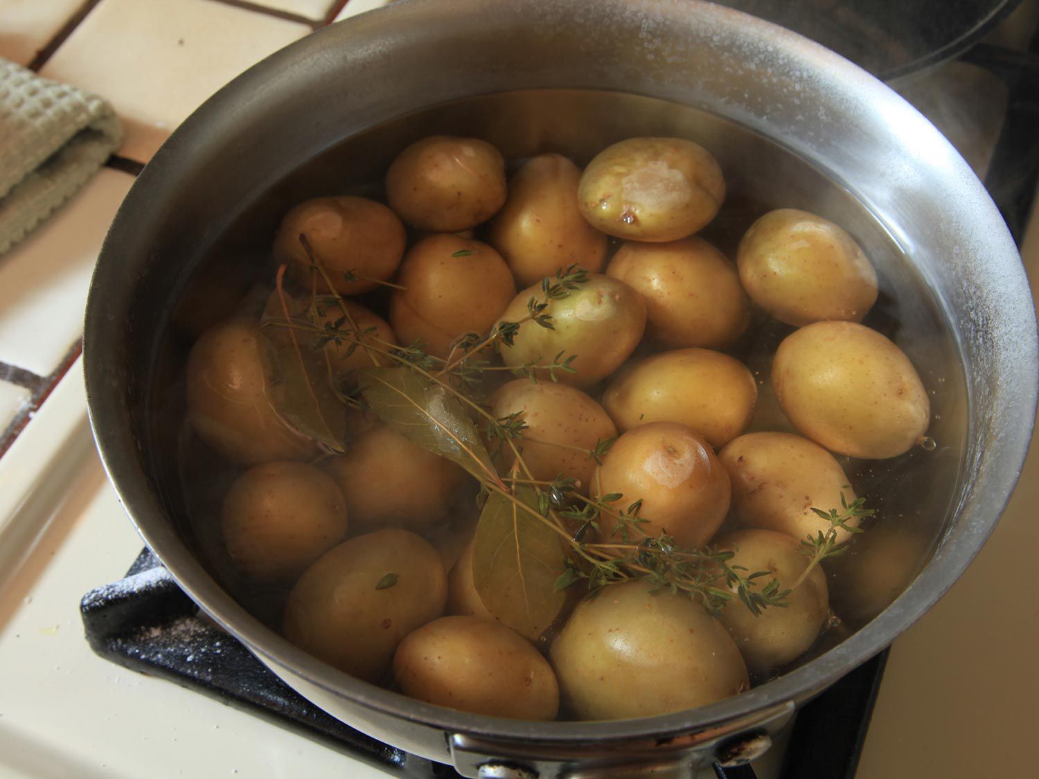 Fresh thyme sprigs infusing pot of water with small new potatoes