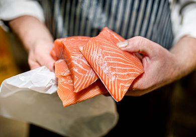 Person holding several fillets of raw salmon with a white bag nearby