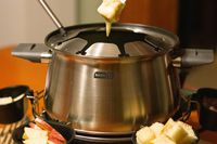 a person dipping bread into the cheese in the fondue pot