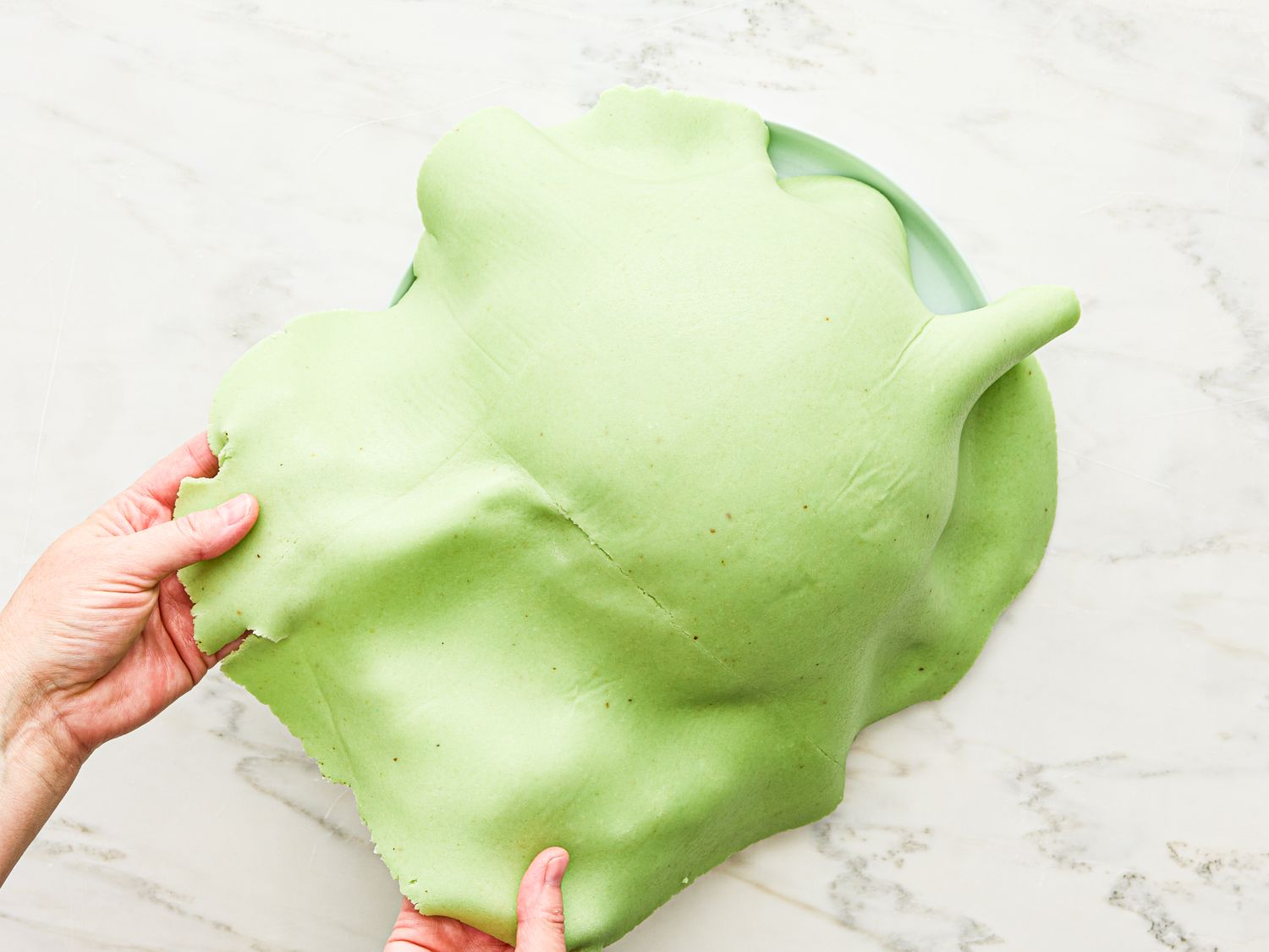 Hands holding green fondant draped for cake decoration