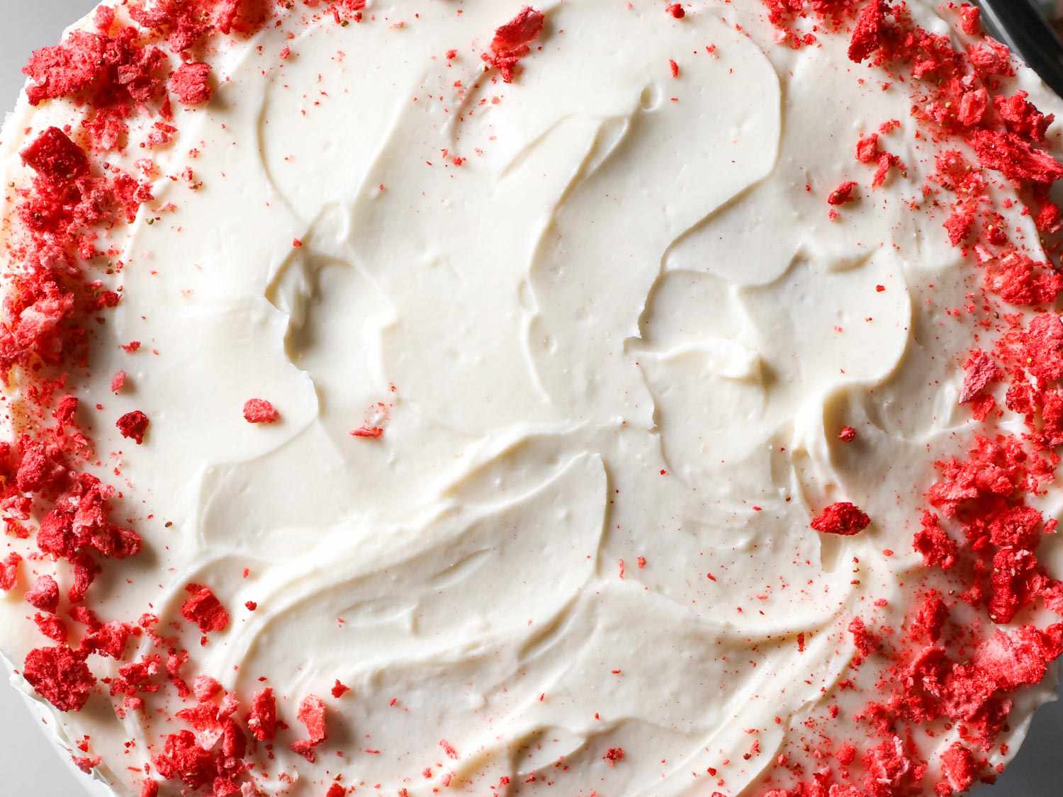 Overhead shot of strawberry layer cake with cream cheese frosting, ringed by crushed freeze-dried strawberries.