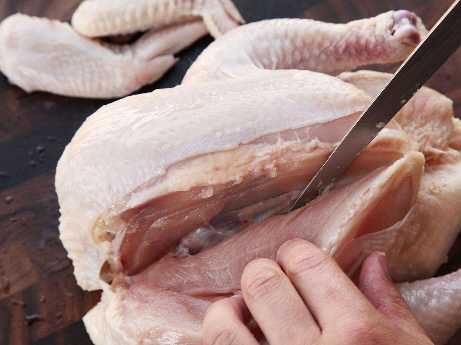 A boning knife slicing off a chicken breast from the body of a whole chicken.