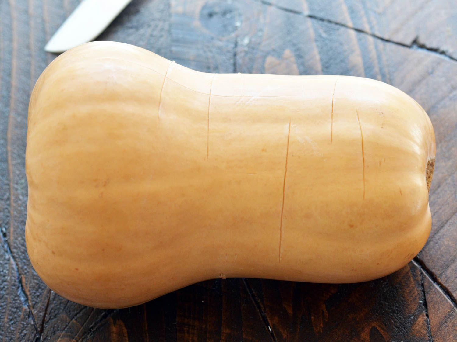 A butternut squash with shallow slices on its skin, about to be microwaved to make peeling easier. 