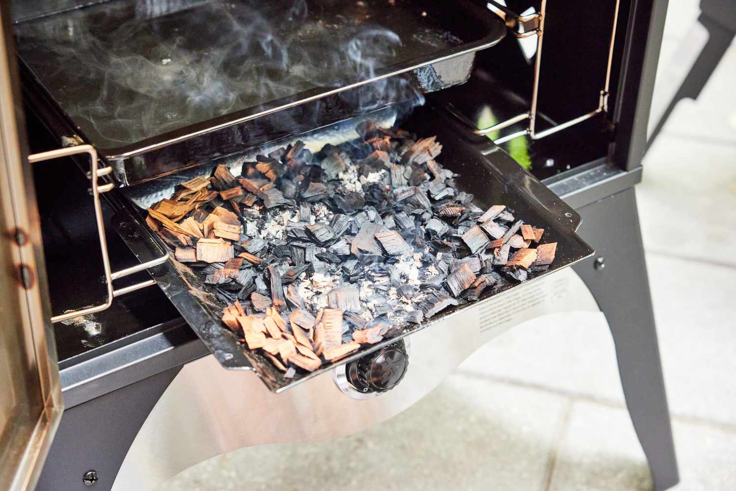A closeup of the wood tray on a propane smoker, filled with burning wood chips