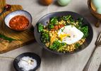 A bowl of stir-fried farro with garlicky kale and a poached egg, served with a ramekin of sambal oelek and a pinch bowl of salt.