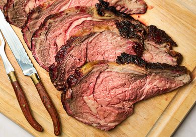 Sliced prime rib on a wooden cutting board with carving utensils nearby