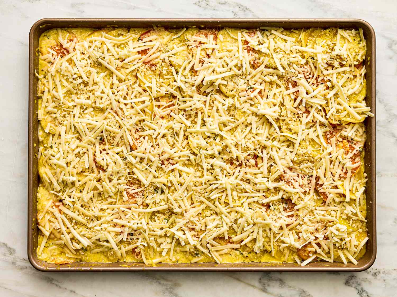 A sheet pan layered with root vegetables grated cheese and breadcrumbs prepared for baking