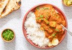 A bowl of tofu tikka masala with rice and garnished with fresh herbs accompanied by naan bread lime wedges and a small bowl of chopped herbs