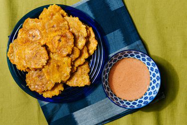 Overhead view of tostones on a blue plate with a blue napkin and bowl of dipping sauce