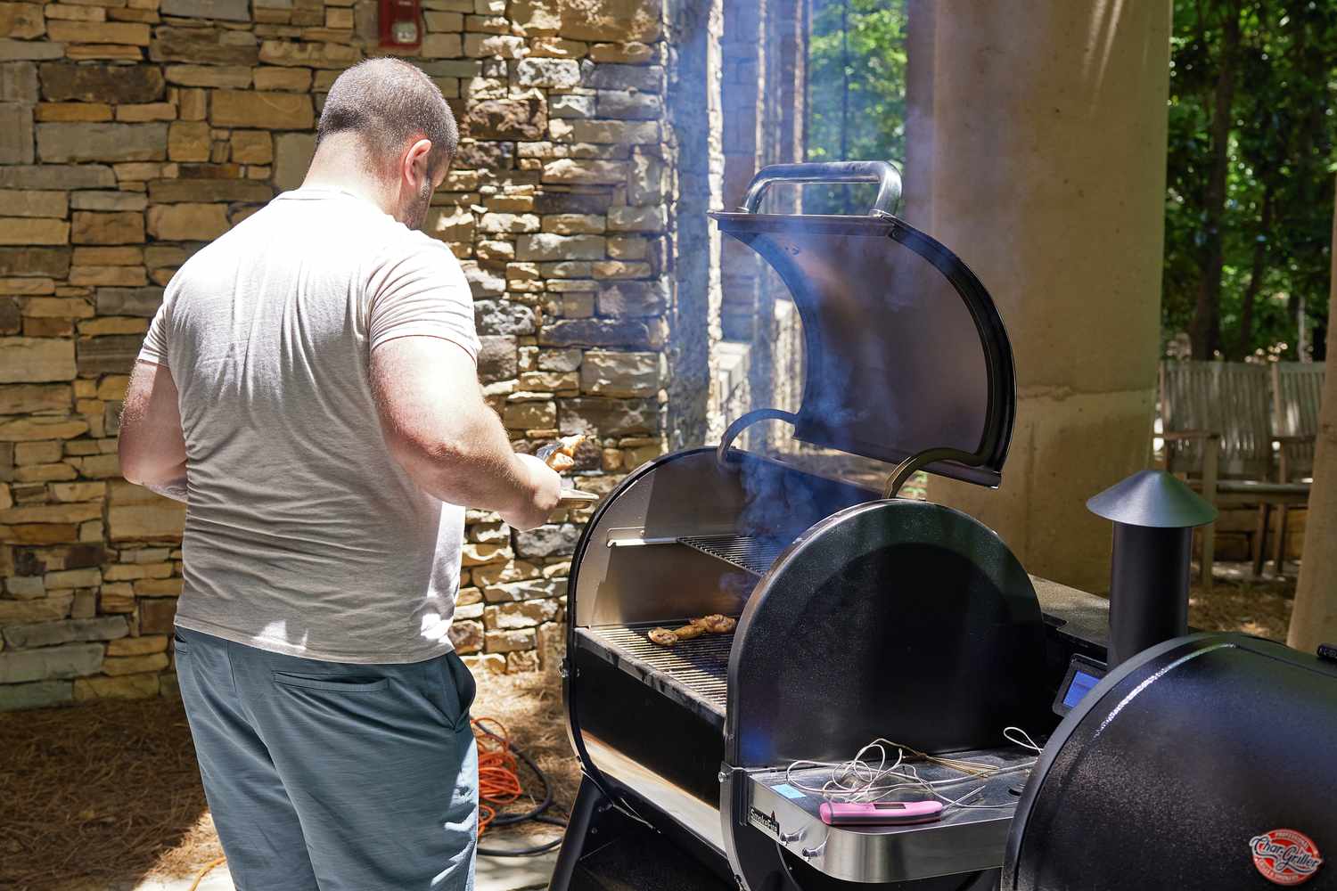 Person pulling cooked wings off a Weber Smokefire EX4 (2nd Gen) Wood Fired Pellet Grill on a patio next to another grill