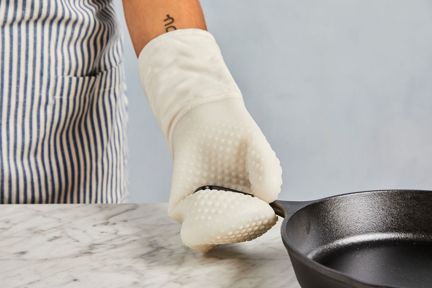 a person using the oxo oven mitt to grab a cast iron pan handle
