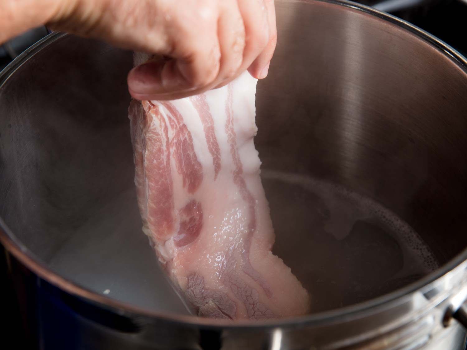 Adding raw pork belly to a pot of starchy rice water for Korean bossam.