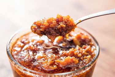 A jar of XO sauce with someone holding a spoon of sauce above the jar. 