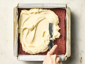 spreading frosting on top of square pan of red velvet brownies 