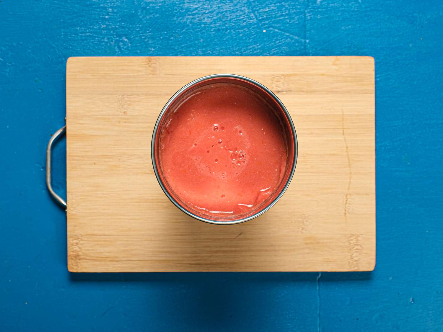 Tomato blended to puree in bowl on wooden board and blue surface