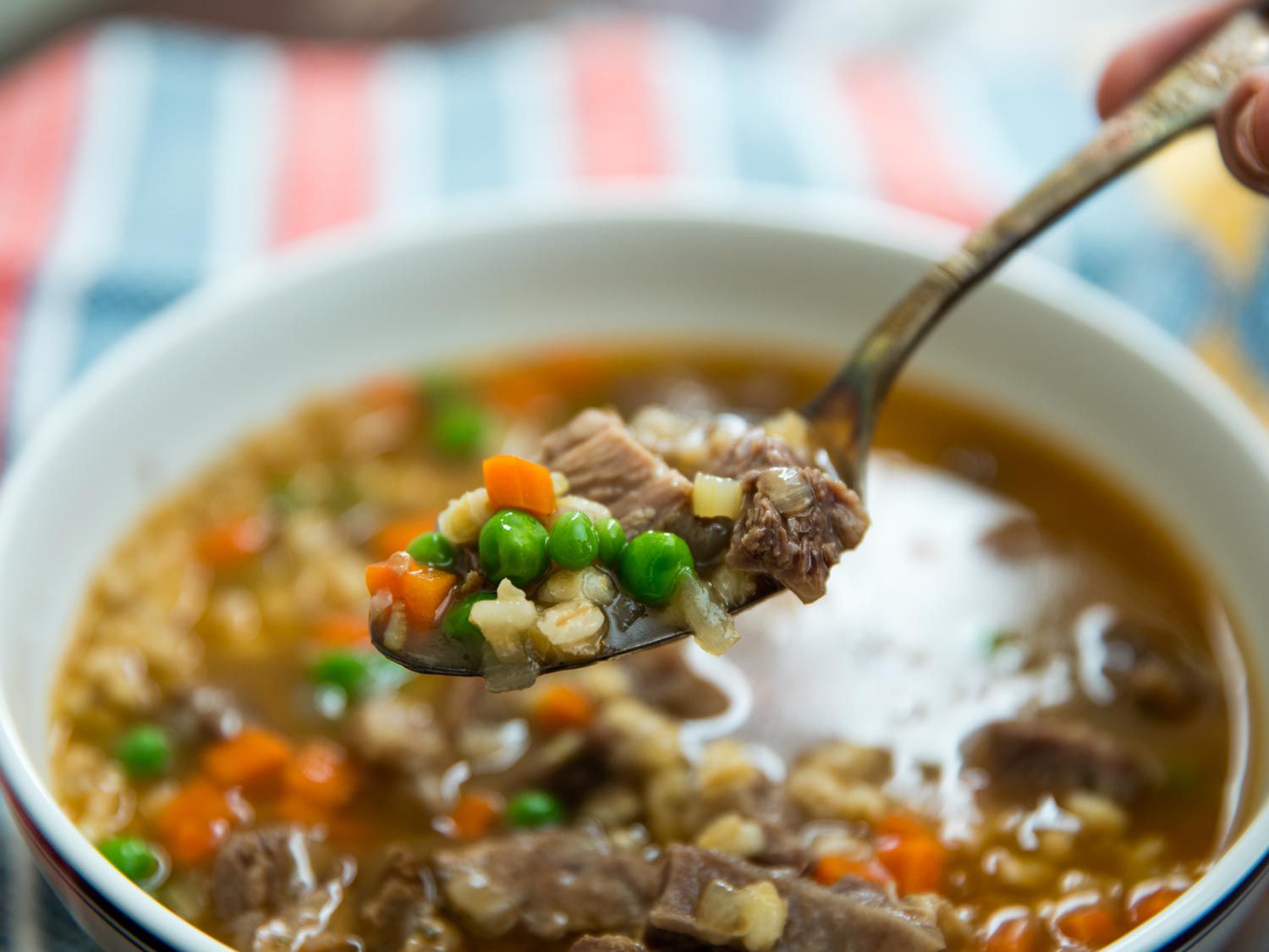 Spoonful of beef barley soup with diced vegetables and peas.