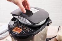 A hand lifting a lid on a modern electric appliance with buttons and display