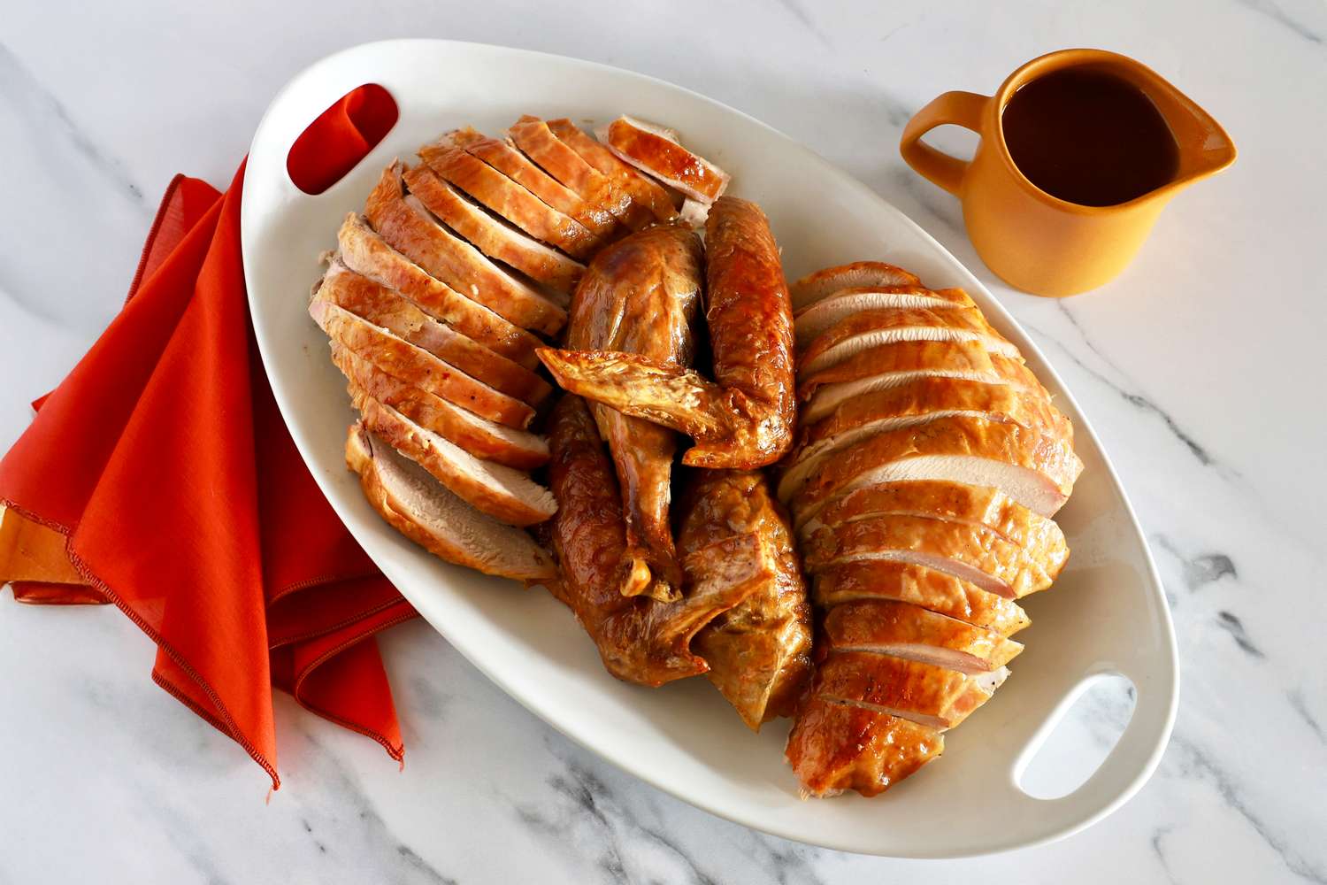 A platter of sliced roasted turkey with a gravy boat on the side