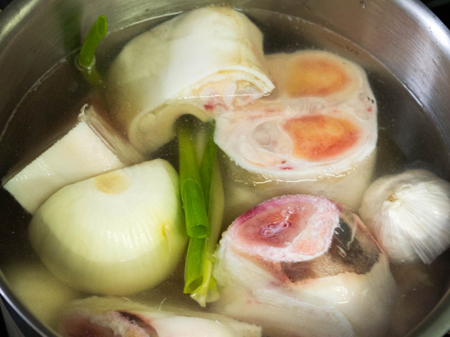 A stainless steel pot holding cut piece of beef bones, water, and vegetables.